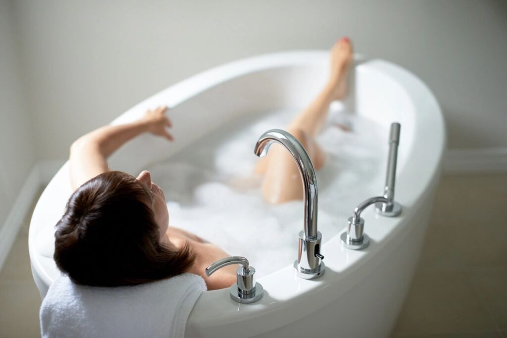 A woman laying in the bathtub with her legs spread wide.