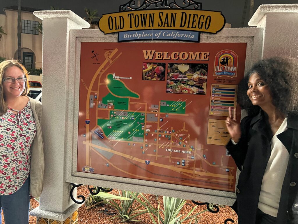 A woman standing next to a sign that says " old town san diego ".
