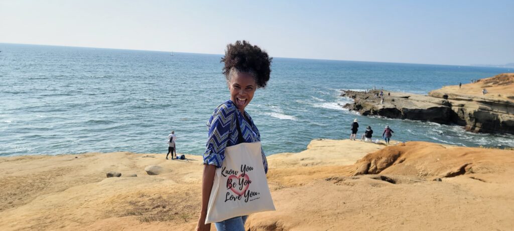 A woman standing on the beach holding a bag.