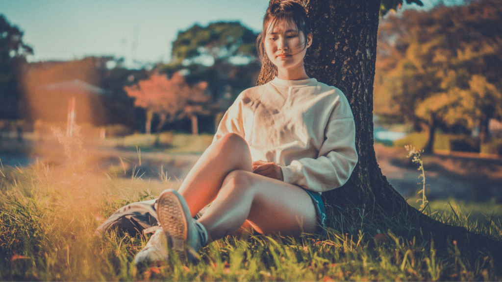 A woman sitting in the grass near a tree.