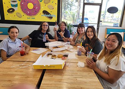 A group of people sitting around a table eating donuts.