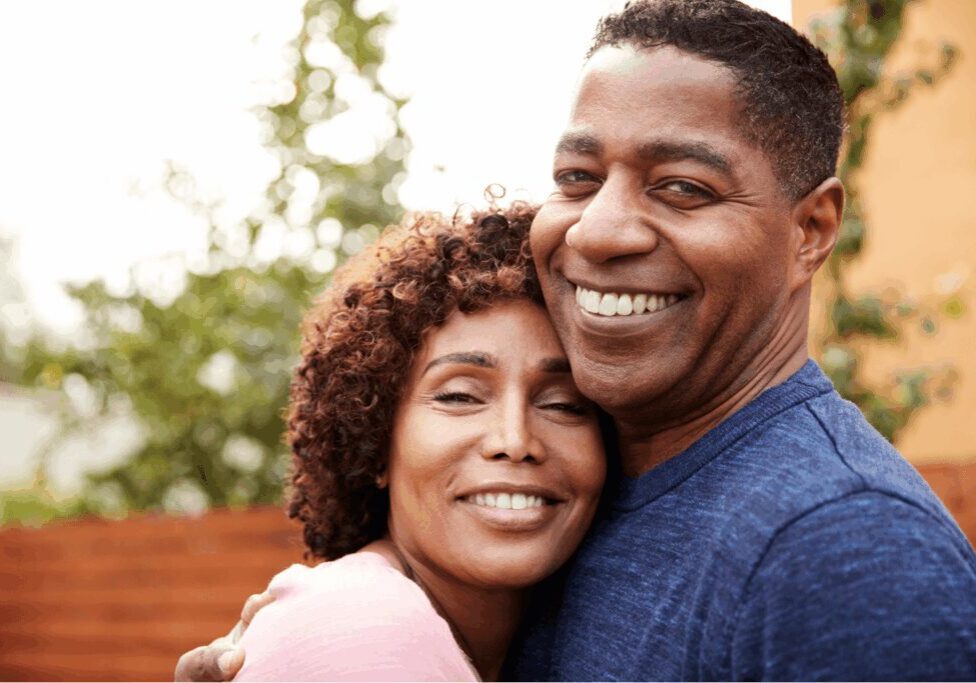 Smiling man and woman embracing outdoors.
